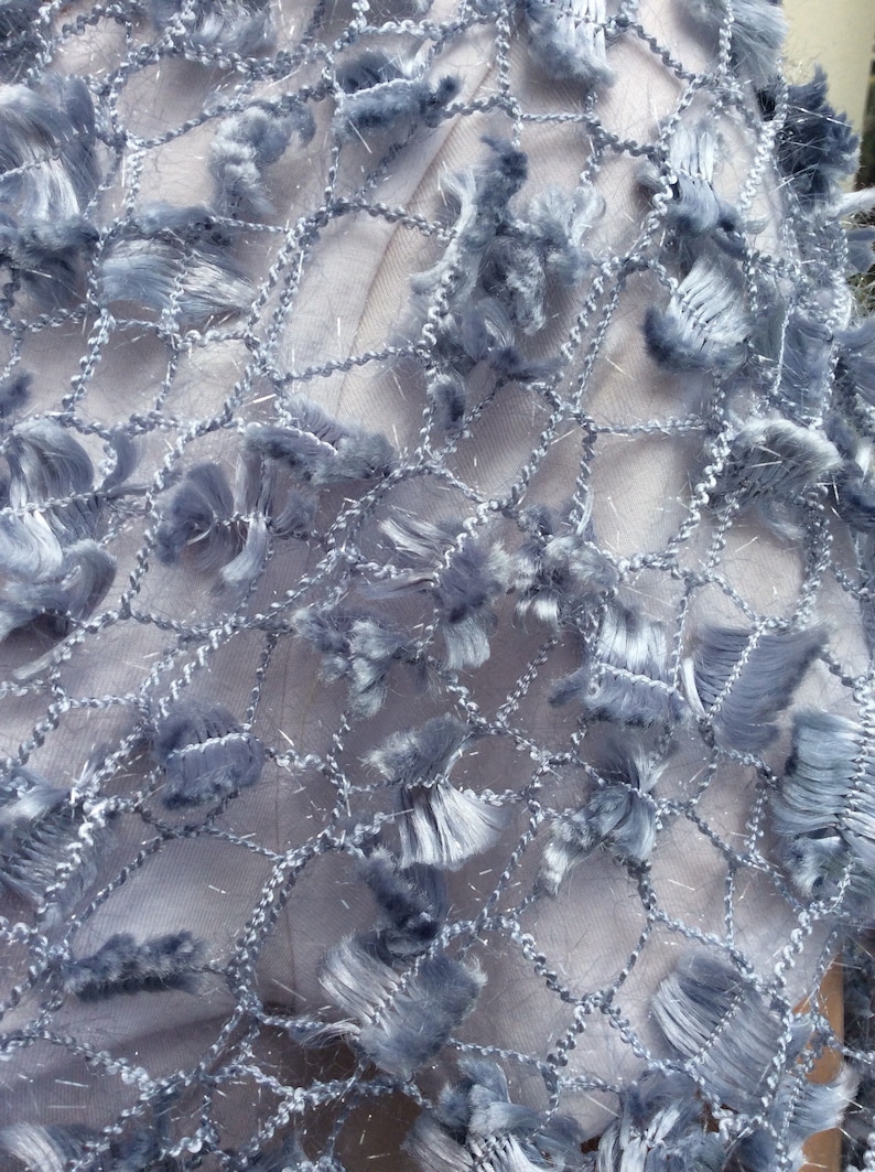May include: A close-up of a light blue fabric with a net-like pattern and fringe details.