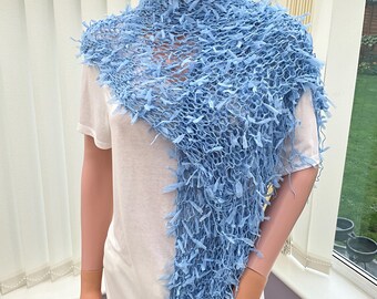 Peut inclure: Une écharpe triangulaire bleu clair présentant une construction en tricot lâche et ajouré avec des éléments de fil texturés ressemblant à des franges. L'accessoire est drapé sur les épaules, affichant un design léger et aéré de couleur bleu ciel.