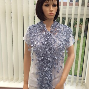 May include: A light blue crocheted shawl with a fringe. The shawl is draped over a mannequin's shoulders.