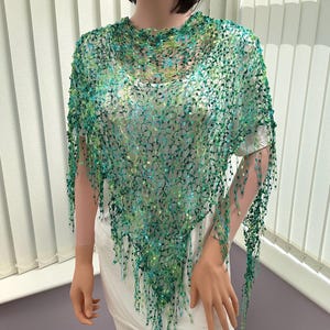 May include: A green and blue crochet shawl with fringe. The shawl is made of a lightweight, open-weave fabric.