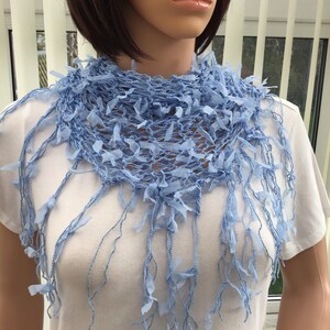 Peut inclure: Une &eacute;charpe en crochet bleu clair avec des franges. L'&eacute;charpe est faite d'un tissu d&eacute;licat &agrave; tissage ouvert et a une texture douce et fluide.