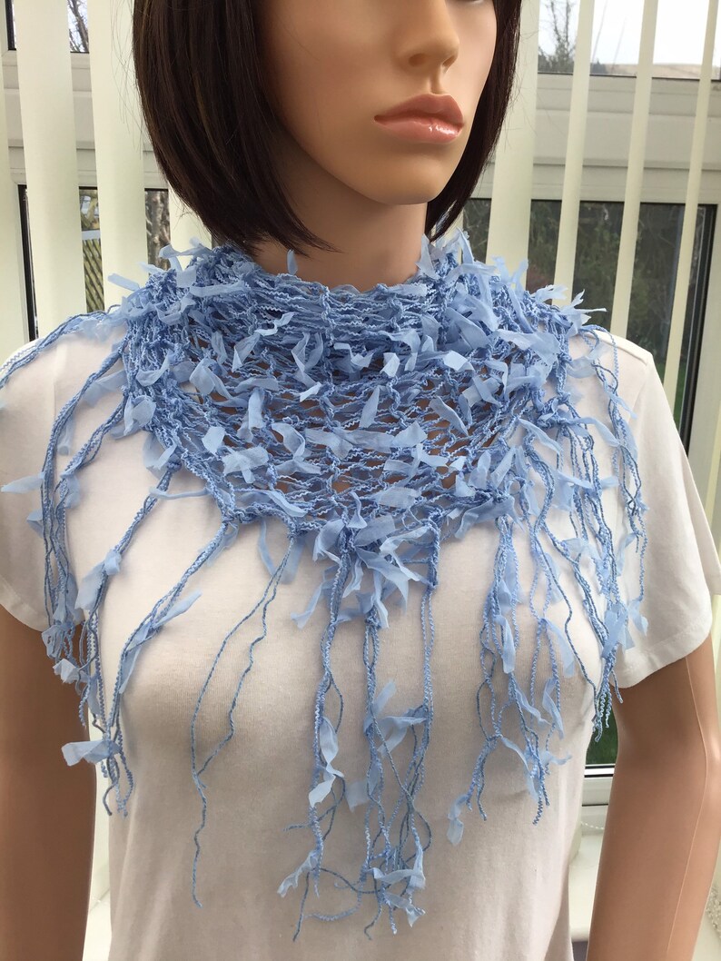 Peut inclure: Une &eacute;charpe en crochet bleu clair avec des franges. L'&eacute;charpe est faite d'un tissu d&eacute;licat &agrave; tissage ouvert et a une texture douce et fluide.