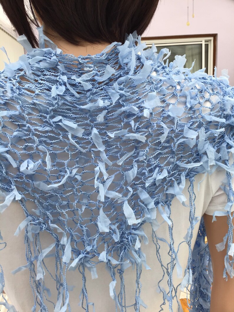 Peut inclure: Un ch&acirc;le en crochet bleu clair avec une bordure en franges. Le ch&acirc;le est fait d'un tissu d&eacute;licat et ajour&eacute;.