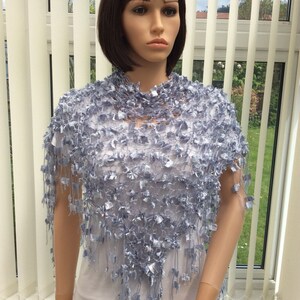 May include: A light blue crocheted shawl with a fringe border. The shawl is made of a delicate, open-weave fabric and has a flowing, elegant design.