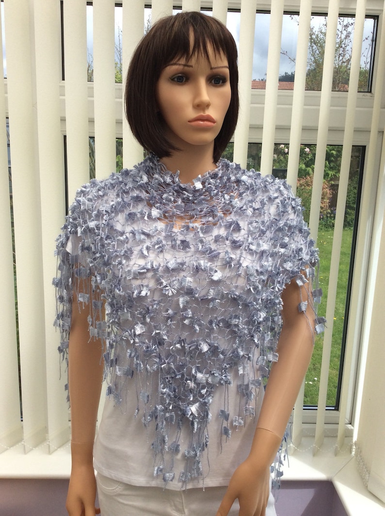 May include: A light blue crocheted shawl with a fringe border. The shawl is made of a delicate, open-weave fabric and has a flowing, elegant design.