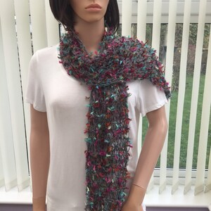 May include: A gray scarf with colorful threads woven throughout. The scarf is made of a soft, lightweight material and has a fringed edge.