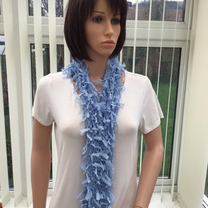 Peut inclure: Une &eacute;charpe bleu clair en tissu crochet&eacute; doux avec une bordure frang&eacute;e. L'&eacute;charpe est drap&eacute; autour du cou d'un mannequin.