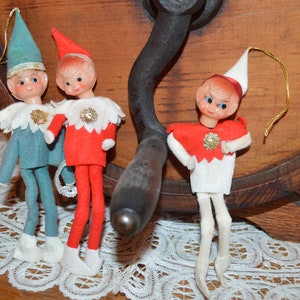 Peut inclure: Quatre décorations d'elfes de Noël vintage avec des vêtements en feutre rouge et blanc et des visages peints. Les elfes sont suspendus à une roue en bois.