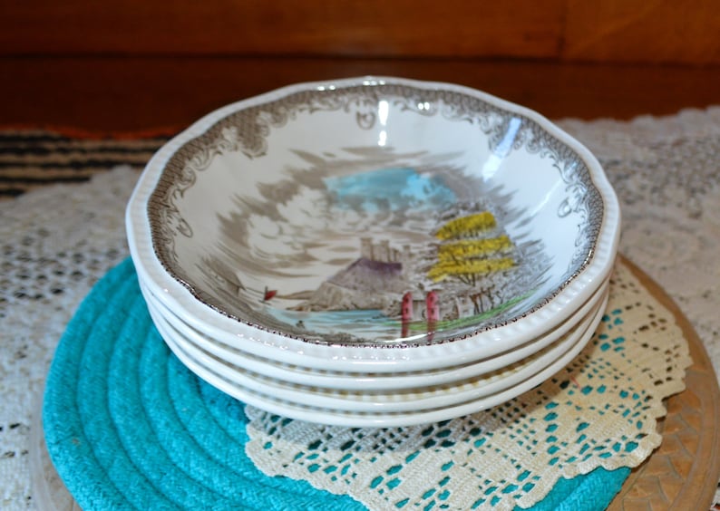 May include: A set of four white ceramic bowls with a brown and gray floral pattern. The bowls feature a scene of a castle and trees by a body of water.