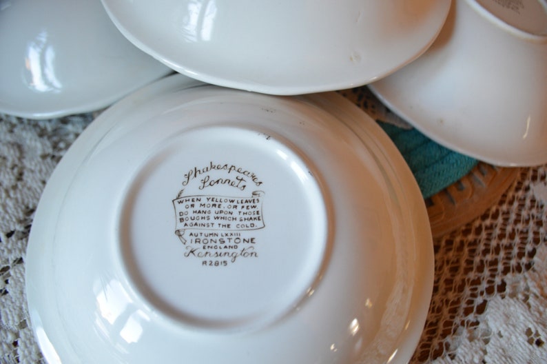 May include: White ceramic saucer with a brown Shakespeare's Sonnets quote and Ironstone Kensington logo. The quote reads: "WHEN YELLOW LEAVES ON MORE.OR FEW DO HANG UPON THOSE BOUGHS WHICH SHAKE AGAINST THE COLD. AUTUMN LEA IRONSTONE Kensington 2815"