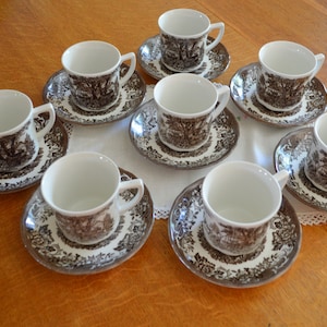 May include: A set of eight brown and white teacups and saucers with a floral pattern. The cups and saucers are arranged in a circle on a wooden table.