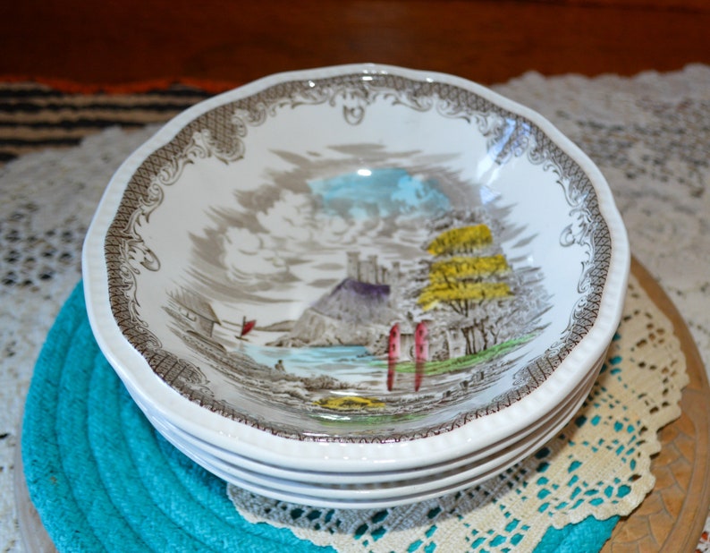 May include: A set of four white ceramic bowls with a brown and gray floral pattern. The bowls feature a scene of a castle on a hill with a lake and trees.