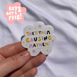 May include: A white cloud-shaped sticker with the text "THEY/THEM CAUSING MAYHEM!" in black, yellow, and purple. The sticker has star and dot designs. A pink cloud-shaped sticker with the text "BUY 3 GET 1 FREE!" is also visible.