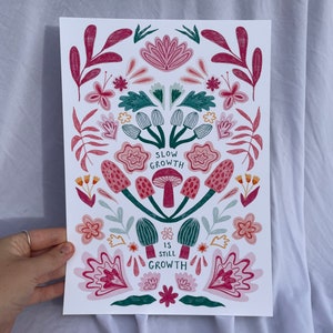 Pu&ograve; includere: Una stampa floreale colorata con uno schema di colori verde, rosa e rosso. La stampa presenta funghi e il testo "Slow Growth is Still Growth".