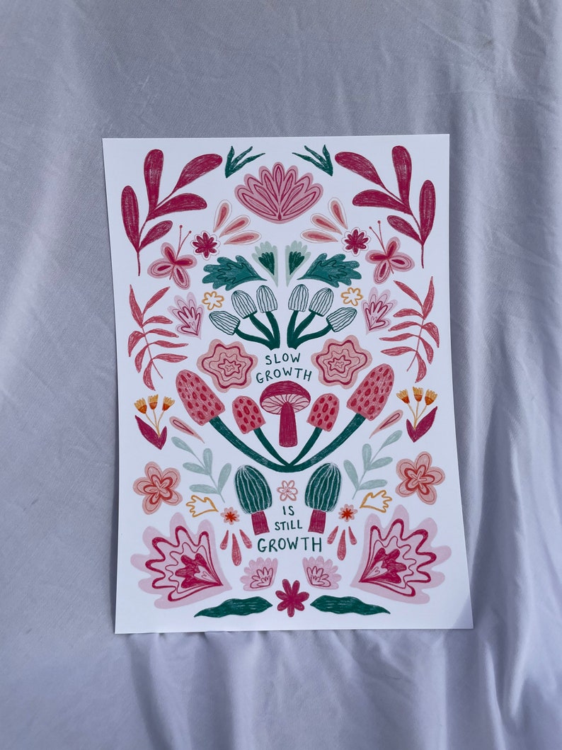 Pu&ograve; includere: Uno sfondo bianco con un design floreale rosa, verde e giallo. Il design presenta funghi con il testo "Slow Growth is Still Growth".
