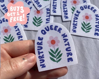 May include: White sticker with a pink flower and the words "NURTURE QUEER NATURE" in blue. The sticker has an arched shape. A pink speech bubble with the text "BUY 3 GET 1 FREE!" is in the upper left corner.