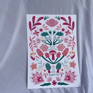 Pu&ograve; includere: Una stampa bianca con un design floreale in tonalit&agrave; rosa, verde e rosso. La stampa presenta funghi con il testo "Slow Growth is Still Growth".