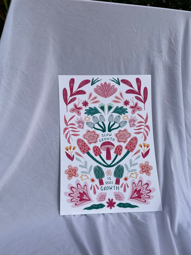 Pu&ograve; includere: Una stampa bianca con un design floreale in tonalit&agrave; rosa e verde. La stampa presenta funghi e il testo "Slow Growth is Still Growth".