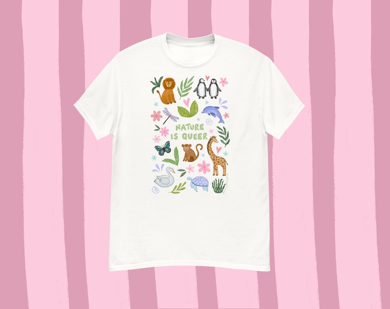 May include: White t-shirt with a colorful illustration of various animals, including a lion, penguins, and a giraffe. The text "NATURE IS QUEER" is printed in a playful font. The design features butterflies, flowers, and leaves.
