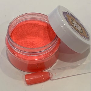 May include: A small clear jar filled with bright orange nail dip powder. A clear plastic applicator is next to the jar.