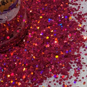 May include: A close-up of a pile of iridescent pink glitter with a variety of sizes and shapes. The glitter has a holographic finish that shimmers in different colors.