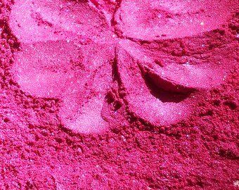 May include: Close-up of a pink glitter powder with a butterfly-shaped design. The glitter is fine and sparkly, creating a shimmering effect.
