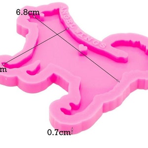 May include: A bright pink silicone mold shaped like a dog with a curled tail. The mold features the embossed text ANGEL WINGS and a small heart shape. Measurements indicated on the mold are 6.8 cm in length, 4.3 cm in width, and 0.7 cm in depth.