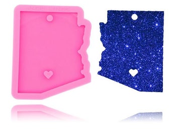 Könnte beinhalten: Rosa Silikonform in Form des Bundesstaates Arizona mit einem kleinen Herz-Ausschnitt. Die Form befindet sich neben einer mit blauen Glitzer besetzten Arizona-Form mit einem Herz-Ausschnitt.