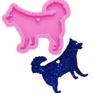 May include: A pink silicone mold shaped like a dog with the text ANGEL WINGS and a small heart embossed on the surface, accompanied by a dark blue glittery dog-shaped cutout that matches the mold's silhouette and features a small heart cutout.