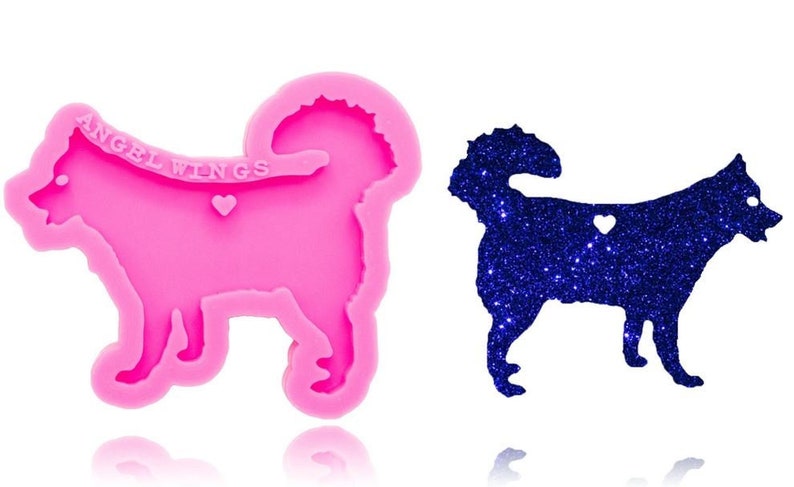 May include: A pink silicone mold in the shape of a dog with a curled tail, featuring the text ANGEL WINGS and a small heart cutout. Beside it is a dark blue glittery dog-shaped cutout with a heart-shaped hole in the center of its body.
