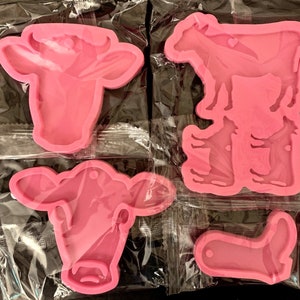 May include: Four pink silicone molds for crafting. The molds are shaped like a cow head, a cow standing, a cow head, and a boot.