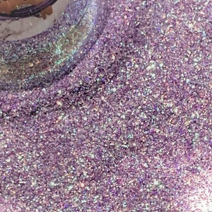 May include: Close-up of iridescent purple glitter with a subtle shimmer. The glitter is fine and evenly distributed, creating a sparkling effect.