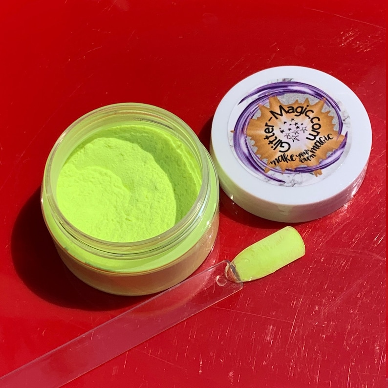 May include: A small jar of bright neon green glitter powder with a clear lid. The jar is labeled "Glitter Magic, Make your own magic". A clear plastic applicator stick with a dab of the glitter on the end is next to the jar.