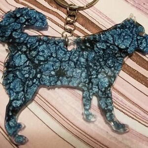 May include: A dog-shaped keychain made of resin with a metallic blue and black marbled finish. The canine silhouette features a textured, swirling pattern of deep blue and dark ink-like veins throughout the body, attached to a silver metal ring.