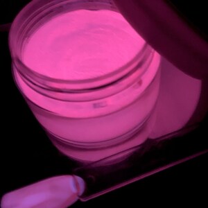 May include: A clear jar filled with a bright pink glow-in-the-dark powder. The powder is used for nail art and is shown with a small brush.