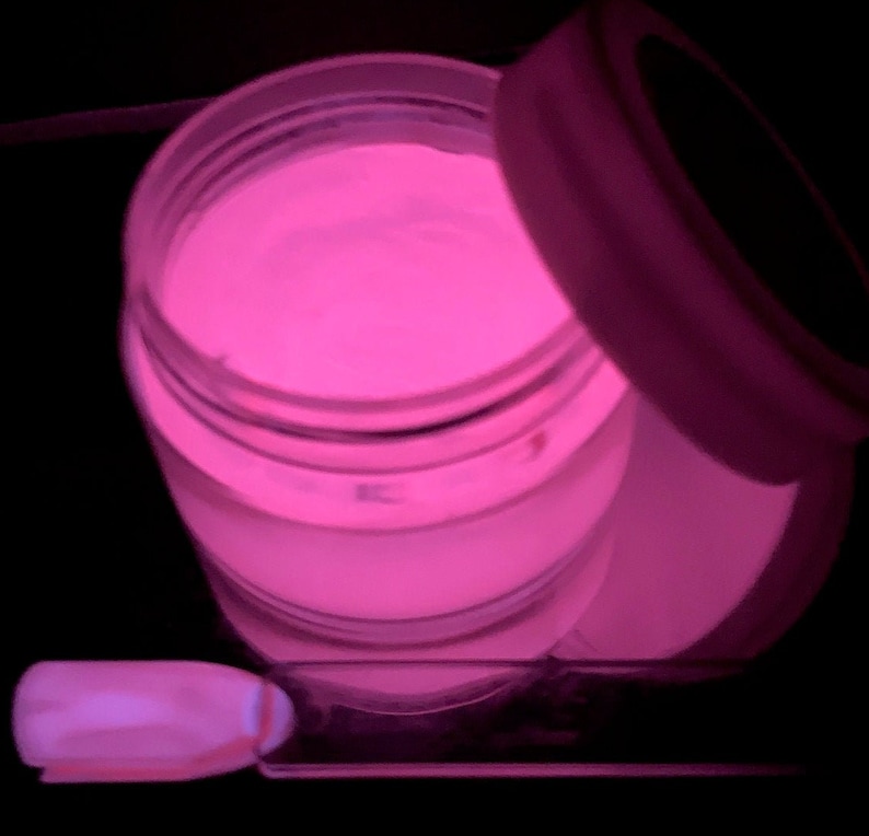 May include: A small jar of pink glow-in-the-dark nail powder. The jar is open and the powder is visible inside. A small nail brush is also visible in the image.
