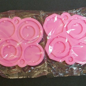 May include: Two pink silicone molds for making jewelry. One mold has four round shapes with holes for earrings. The other mold has five geometric shapes with holes for pendants.