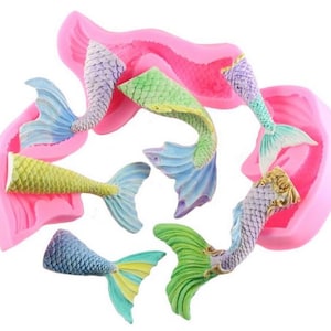 May include: Pink silicone mold with five mermaid tail shapes. The tails are in various colors, including green, blue, purple, and yellow.
