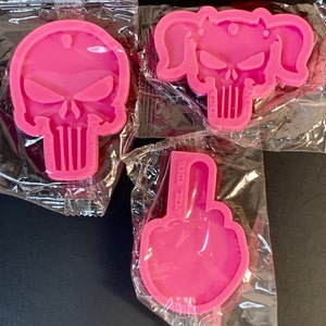 May include: Three pink silicone moulds for making resin crafts. The moulds are shaped like a skull, a skull with pigtails, and a middle finger.