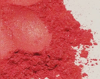 May include: A close-up of a pile of bright red glitter. The glitter is fine and sparkly, and it is scattered on a white surface.