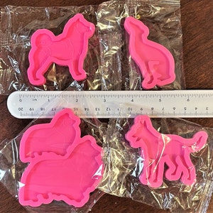 May include: Four pink silicone molds shaped like different dog breeds. The molds are packaged in clear plastic bags.