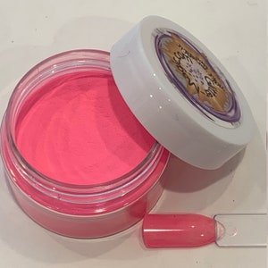 K&ouml;nnte beinhalten: Ein kleines, klares Glas gef&uuml;llt mit leuchtend pinkfarbenem Nagelpulver. Das Glas hat einen wei&szlig;en Deckel mit dem Text "Glamnetic" in einem violetten Kreis mit einem goldenen Stern.
