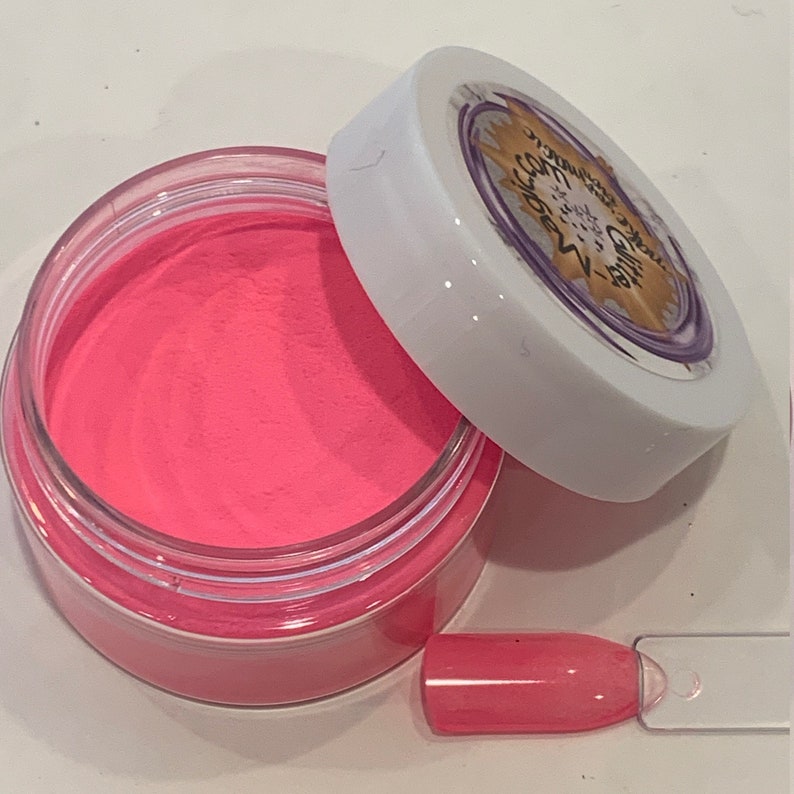 K&ouml;nnte beinhalten: Ein kleines, klares Glas gef&uuml;llt mit leuchtend pinkfarbenem Nagelpulver. Das Glas hat einen wei&szlig;en Deckel mit dem Text "Glamnetic" in einem violetten Kreis mit einem goldenen Stern.