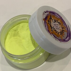 May include: A small jar of neon yellow glitter powder with a white lid. The lid has a purple and gold sticker with the text "Glitter Magic" and "Worn Magic" on it.