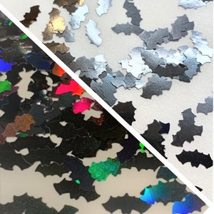 May include: Two different types of iridescent glitter in the shape of bats. One type is black with rainbow iridescent glitter and the other is silver with a holographic finish.