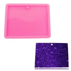 May include: Pink silicone mold for making resin crafts. The mold is rectangular with a hole at the top for a pendant or charm. The mold is shown with a purple glitter background.