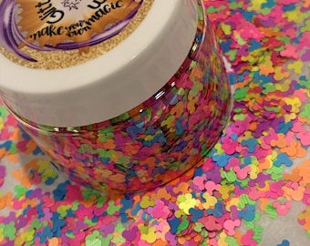 May include: A clear jar filled with colorful Mickey Mouse shaped glitter. The jar has a white lid with a gold and purple label that reads "Glitter Magic - Make your own magic".