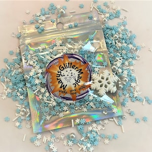 May include: A clear plastic bag filled with blue and white snowflake sprinkles, white pearl sprinkles, and white sticks. The bag has a label that says "Glitter Magic" with a starburst design.