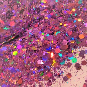 May include: A close-up of iridescent pink glitter with a variety of shapes and sizes. The glitter is scattered on a light pink surface.