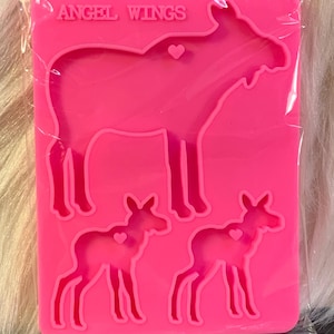 May include: Pink silicone mold with three moose shapes. The largest moose is standing, while the two smaller moose are standing with their heads turned to the side. The mold has the words "ANGEL WINGS" at the top.